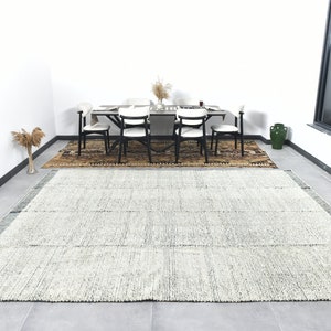 May include: A white and blue striped rug with a subtle pattern. The rug is laid out on a tiled floor in a room with a dining table and chairs.