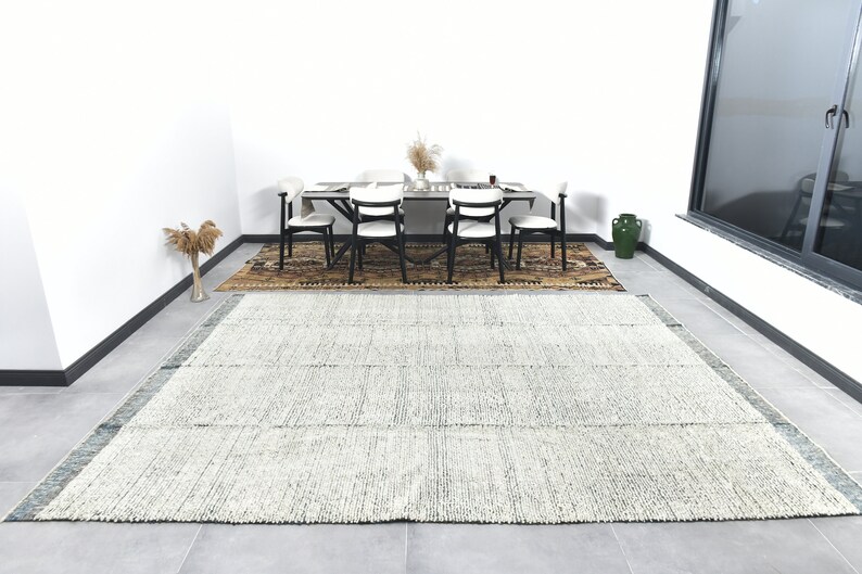 May include: A white and blue striped rug with a subtle pattern. The rug is laid out on a tiled floor in a room with a dining table and chairs.