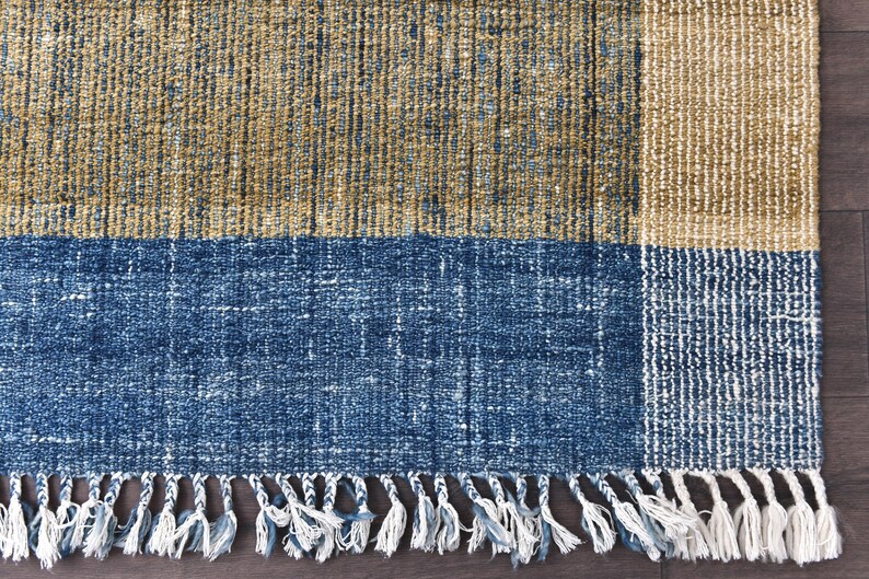 Handwoven area rug featuring geometric color blocks in rich navy blue, warm golden yellow, olive green and natural beige tones. This modern Turkish kilim style rug has a textured flat weave with white fringe edges, perfect for bohemian or Scandinavian interiors. Natural fiber construction creates an eco-friendly floor covering.