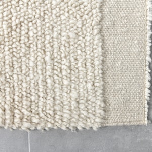 May include: Close-up of a cream-colored rug with a textured, fluffy surface. The rug has a woven edge.