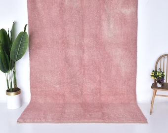 May include: A soft, pink shag rug with a subtle, faded pattern. The rug is hanging on a white wall and has a white border.