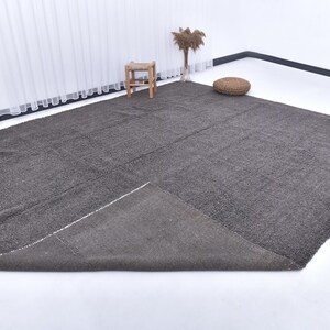 May include: A dark gray area rug with a textured surface. The rug is folded in half and laid out on a white surface.