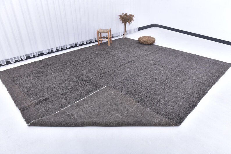 May include: A dark gray area rug with a textured surface. The rug is folded in half and laid out on a white surface.