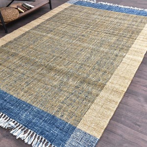 Handwoven area rug featuring geometric color blocks in rich navy blue, warm golden yellow, olive green and natural beige tones. This modern Turkish kilim style rug has a textured flat weave with white fringe edges, perfect for bohemian or Scandinavian interiors. Natural fiber construction creates an eco-friendly floor covering.