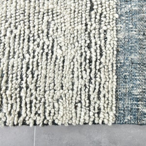 May include: Close-up of a white and gray textured rug with a blue border. The rug has a unique, hand-woven look.