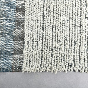 May include: Close-up of a white and blue woven rug with a textured surface. The rug has a fringe border.