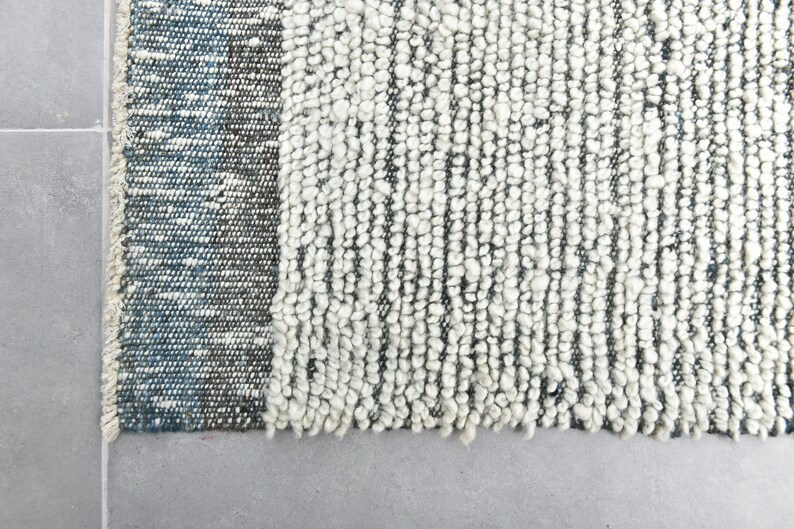 May include: Close-up of a white and blue woven rug with a textured surface. The rug has a fringe border.