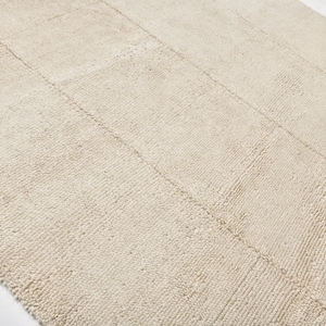 May include: A close-up of a cream-coloured rug with a textured woven pattern. The rug has a subtle sheen and a slightly rough texture.