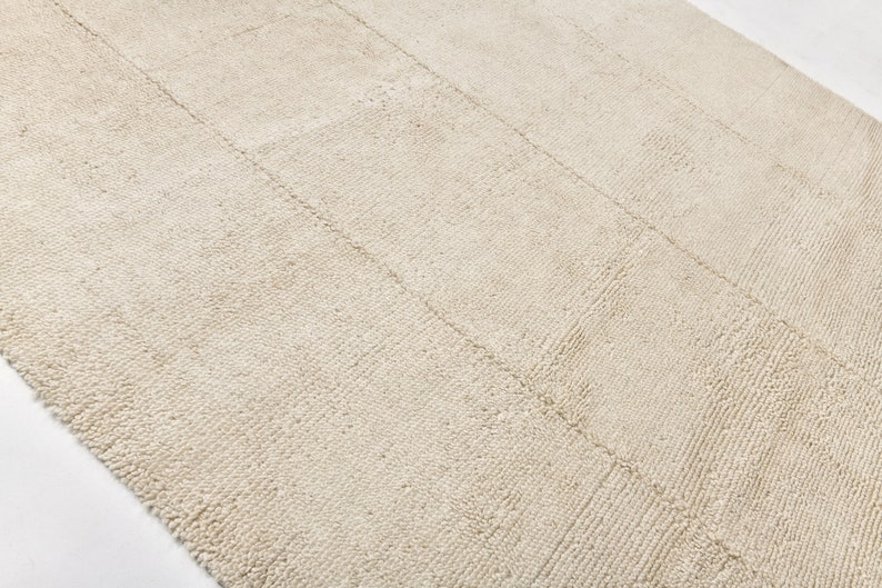 May include: A close-up of a cream-coloured rug with a textured woven pattern. The rug has a subtle sheen and a slightly rough texture.