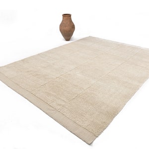 May include: A beige rectangular rug with a textured surface and a subtle pattern. The rug has a woven border.