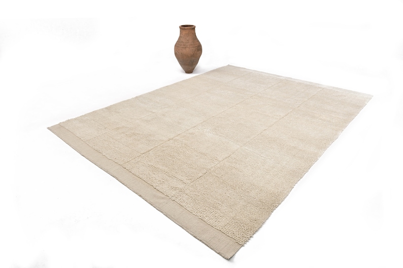 May include: A beige rectangular rug with a textured surface and a subtle pattern. The rug has a woven border.