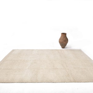 May include: A light beige rectangular rug with a subtle texture. The rug is on a white background with a brown clay pot in the centre.