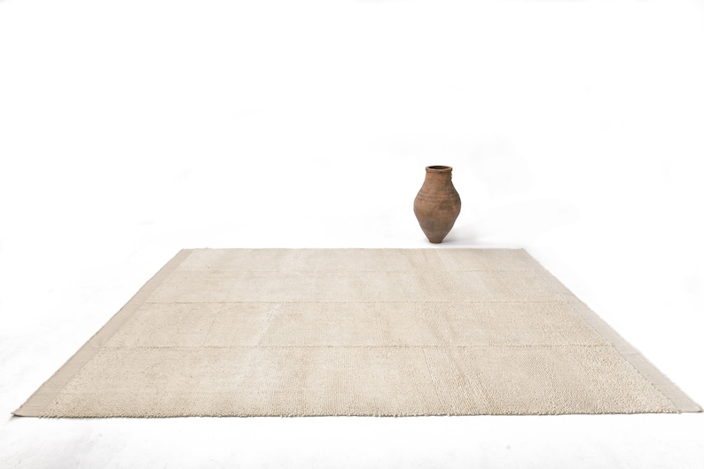 May include: A light beige rectangular rug with a subtle texture. The rug is on a white background with a brown clay pot in the centre.
