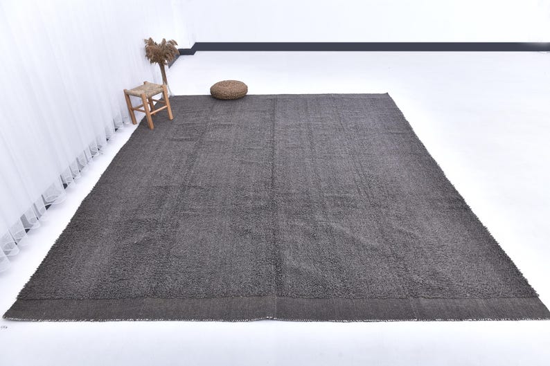 May include: A dark gray shag rug with a subtle texture. The rug is laid out on a white floor in a room with white walls.