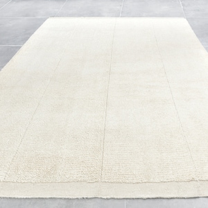 May include: A white, fluffy rug with a subtle texture. The rug has a simple, modern design and is perfect for adding a touch of warmth and comfort to any room.