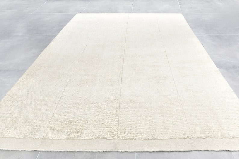 May include: A white, fluffy rug with a subtle texture. The rug has a simple, modern design and is perfect for adding a touch of warmth and comfort to any room.