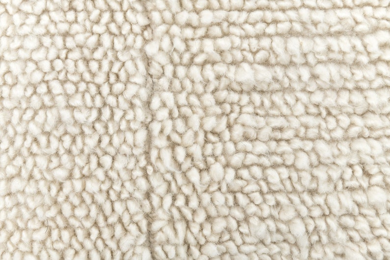 May include: Close-up of a cream-colored, fluffy, textured fabric. The fabric has a soft, fuzzy appearance.