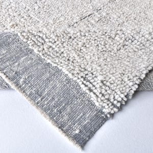 Può includere: Primo piano di un tappeto bianco e grigio con una superficie testurizzata. Il tappeto ha un bordo grigio.