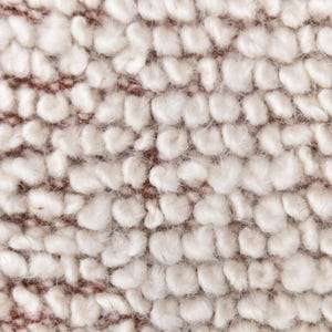 May include: Close-up of a white, fluffy fabric with a textured, bumpy surface. The fabric has a slightly brown hue.