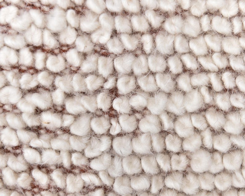 May include: Close-up of a white, fluffy fabric with a textured, bumpy surface. The fabric has a slightly brown hue.