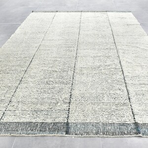 May include: A white and gray area rug with a subtle textured pattern. The rug has a dark gray border.
