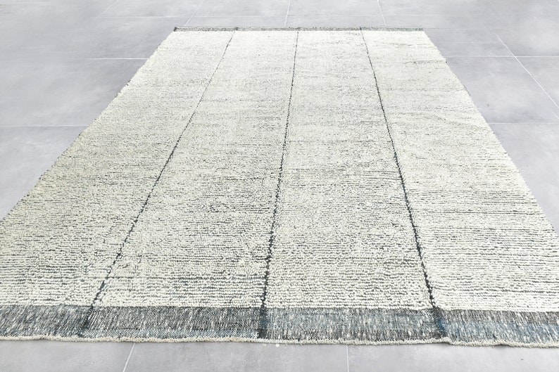 May include: A white and gray area rug with a subtle textured pattern. The rug has a dark gray border.