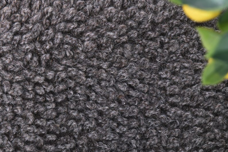 May include: Close-up of a dark gray fuzzy fabric texture. The fabric has a soft, plush feel and a slightly textured surface.