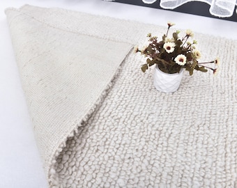 May include: A white fluffy rug with a small white planter with white flowers on top.