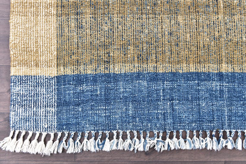 Handwoven area rug featuring geometric color blocks in rich navy blue, warm golden yellow, olive green and natural beige tones. This modern Turkish kilim style rug has a textured flat weave with white fringe edges, perfect for bohemian or Scandinavian interiors. Natural fiber construction creates an eco-friendly floor covering.