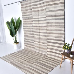Pu&ograve; includere: Un grande tappeto a strisce in tonalit&agrave; beige e bianco &egrave; appeso a un muro. Il tappeto &egrave; realizzato in fibre naturali e ha un aspetto rustico e tessuto a mano.