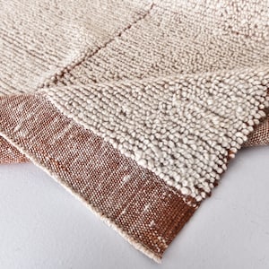 May include: Close-up of a white and brown woven rug with a textured surface. The rug has a fringe border.