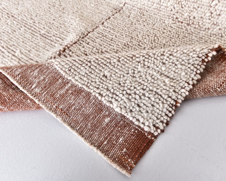 May include: Close-up of a white and brown woven rug with a textured surface. The rug has a fringe border.