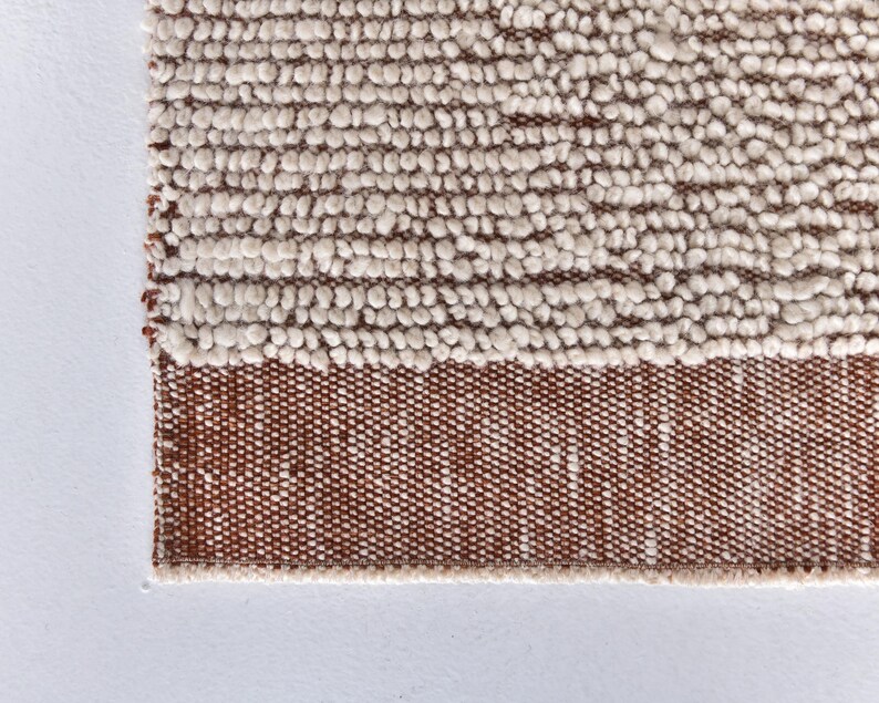 May include: Close-up of a white and brown woven rug with a textured surface. The rug has a fringe border.