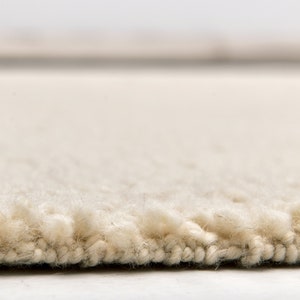 May include: Close-up of a cream-coloured rug with a fluffy texture. The rug has a subtle sheen and a slightly uneven surface.