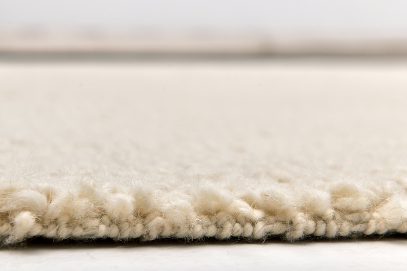 May include: Close-up of a cream-coloured rug with a fluffy texture. The rug has a subtle sheen and a slightly uneven surface.