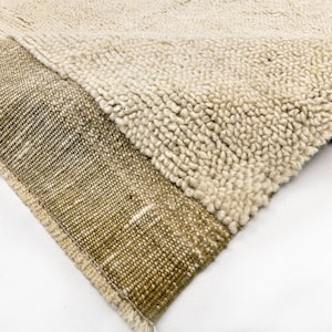 May include: Close-up of a beige and brown woven rug with a textured surface. The rug is folded in half, showing the different colors and textures.