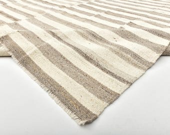 Può includere: Un tappeto tessuto a strisce beige e marrone chiaro alternate. Il bordo del tappeto è sfilacciato e il tessuto sembra essere una fibra naturale. Il tappeto è piegato, rivelando il lato inferiore.
