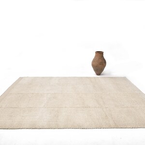 May include: A rectangular beige rug with a textured surface. A brown, aged, ceramic vase sits on a white background. The rug has a simple, geometric design, suitable for a living room or bedroom.