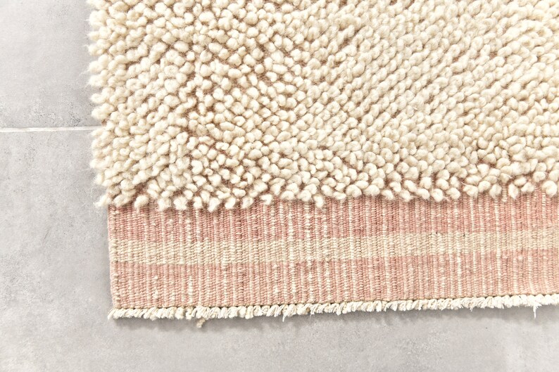 Puede incluir: Una alfombra de color crema con una textura esponjosa y un borde rayado rosa y crema.