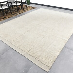 May include: A large, off-white, rectangular rug with a subtle texture. The rug has a border that is slightly darker than the center.