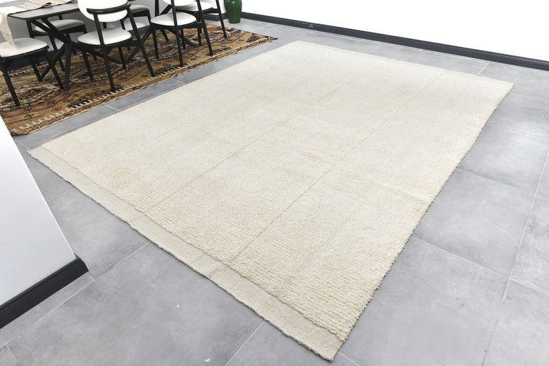 May include: A large, off-white, rectangular rug with a subtle texture. The rug has a border that is slightly darker than the center.