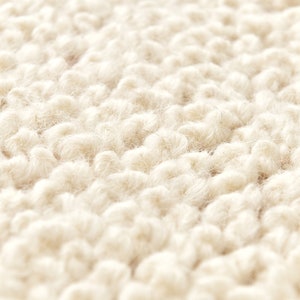 Puede incluir: Primer plano de una alfombra esponjosa de color crema con un tejido texturizado y en bucle.