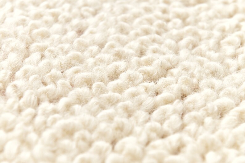 Puede incluir: Primer plano de una alfombra esponjosa de color crema con un tejido texturizado y en bucle.