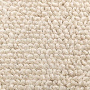 May include: Close-up of a cream-colored, textured fabric. The material has a dense, looped pile, creating a soft, plush appearance. The surface is covered in small, tightly packed loops, giving it a warm and inviting look. The fabric appears to be a type of faux fur or shearling.