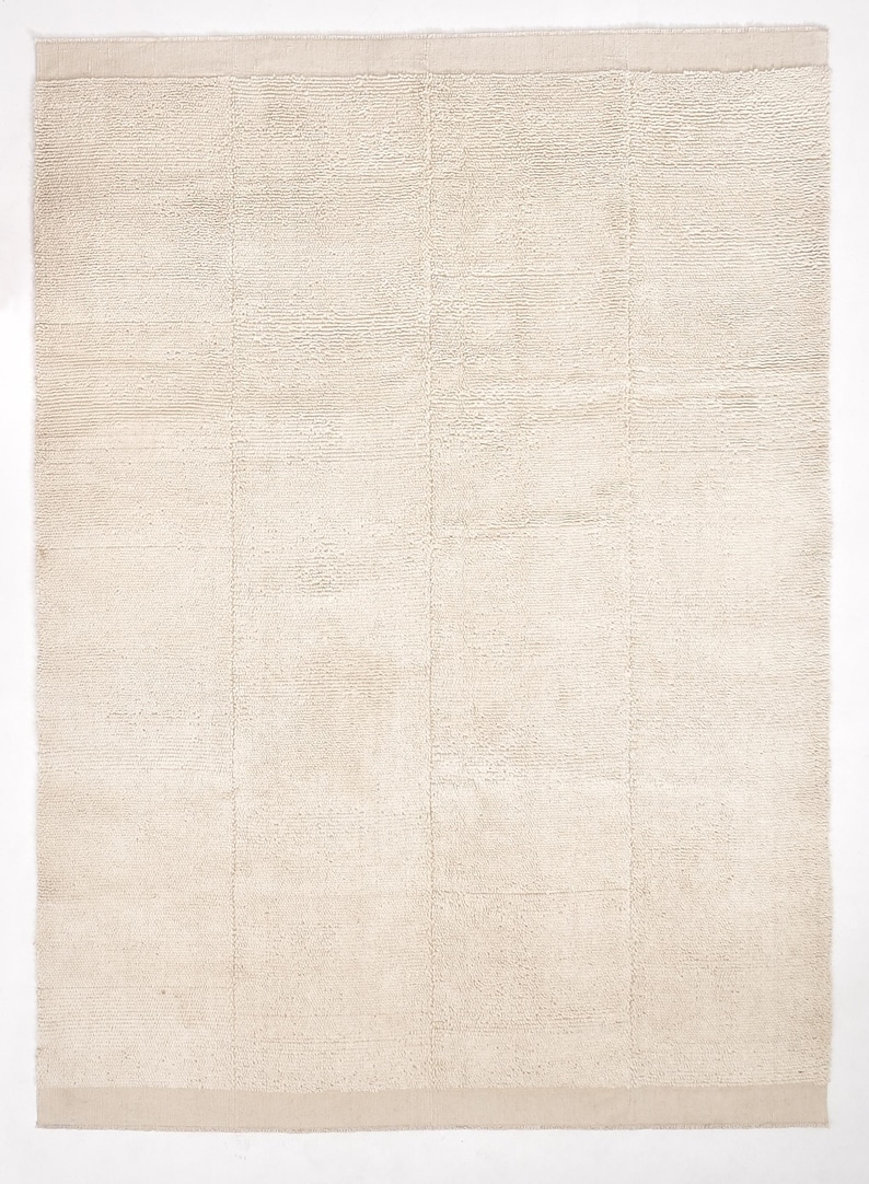 May include: A cream-coloured rug with a subtle woven texture. The rug has a slightly raised border.