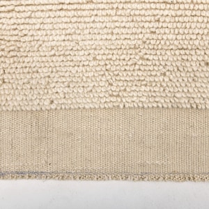 May include: Close-up of a cream-coloured rug with a woven texture. The rug has a fringe border and a cream-coloured backing.