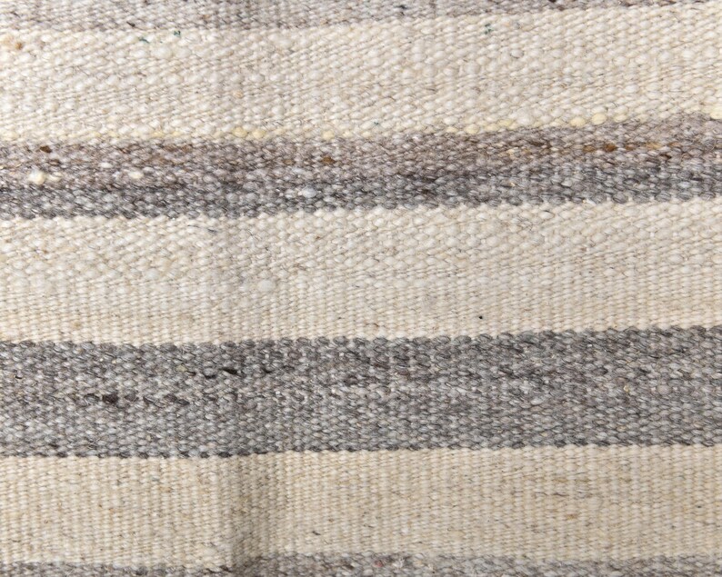 Pu&ograve; includere: Primo piano di un tappeto tessuto con strisce orizzontali in tonalit&agrave; di bianco e grigio.