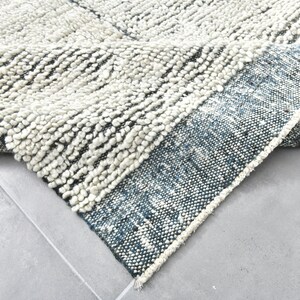 May include: A close-up of a white and blue rug with a textured, fluffy surface. The rug has a fringe border and is folded in half.