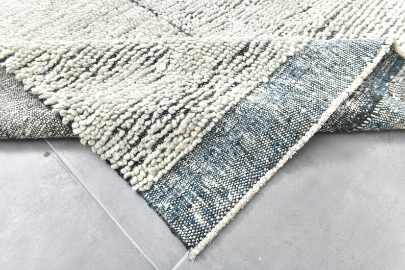 May include: A close-up of a white and blue rug with a textured, fluffy surface. The rug has a fringe border and is folded in half.