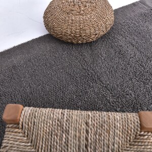 May include: A close-up of a gray, textured rug with a woven wicker stool and a woven wicker ottoman. The stool and ottoman are both in the center of the image.